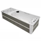 A high-end dual-zone swim spa with a built-in hot tub and waterproof TV screen, set in a modern outdoor patio at sunset, with LED lighting and water features turned on.